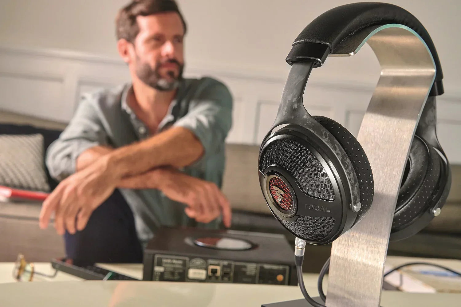 Focal high-end headphones on stand, man relaxing on sofa, premium audio setup at The Source AV